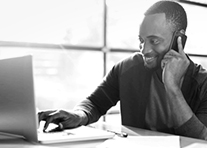 A man is smiling while talking on his cell phone and working on his laptop